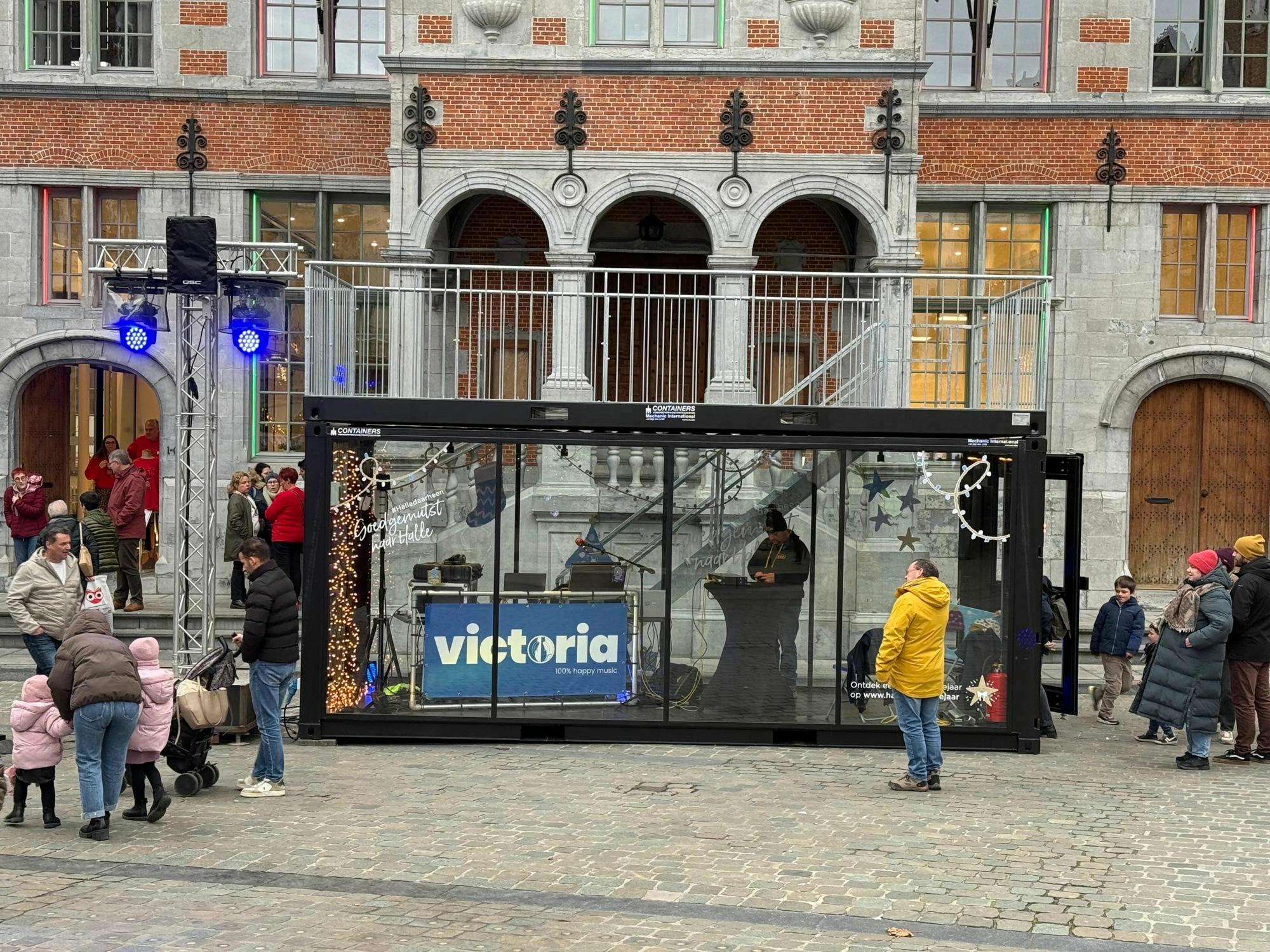 Conteneur vitré avec lettrage adhésif au marché de Noël de Hal, avec vue sur l'hôtel de ville historique.